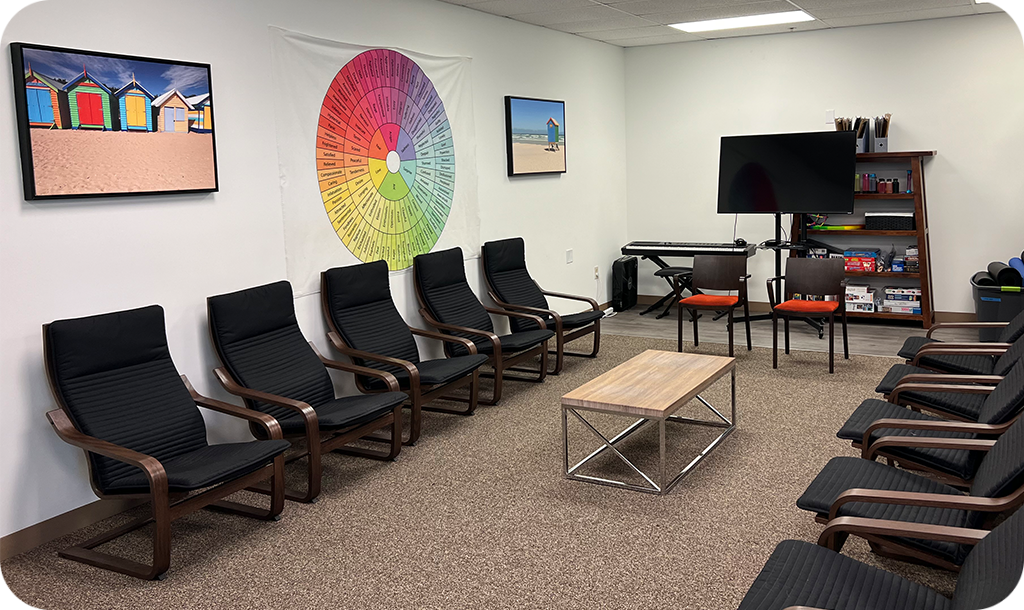 Group room with individual chairs lined up on left and right sides. There's a tv and colorful paintings on the walls.