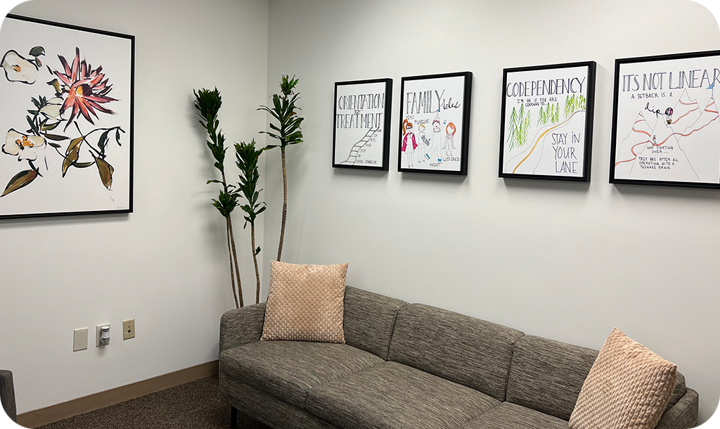 Room with a light brown couch, peach pillows, and paintings on the wall with flowers and insighful messages.